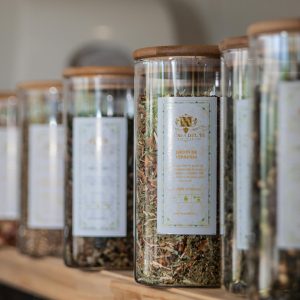 A selection of glass jars filled with herbal teas displayed on an indoor shelf.