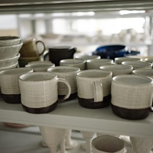 Close-up of artisan-crafted ceramic mugs on a shelf, showcasing pottery craftsmanship.