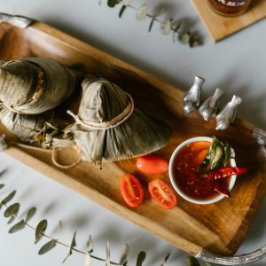 Delicious traditional machang served with spicy chili sauce on a wooden tray, garnished with fresh tomatoes.