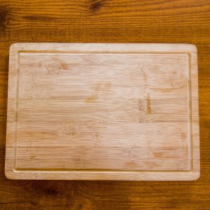 Top view of a natural wooden bamboo chopping board on a textured surface.