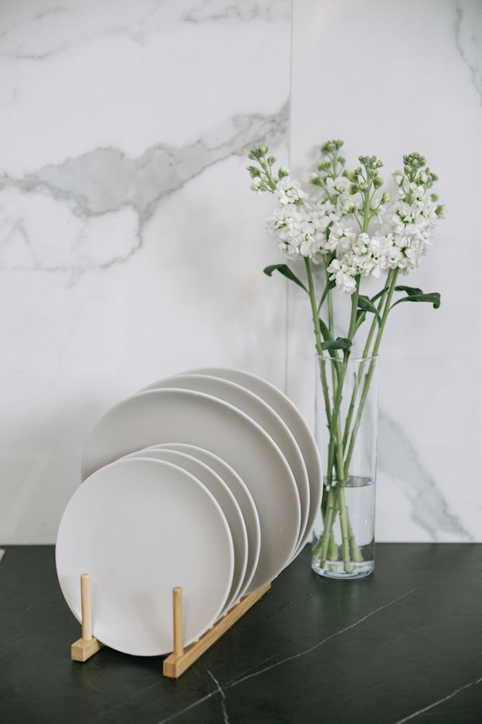 A serene composition of stacked plates with a vase of white flowers against a marble backdrop.